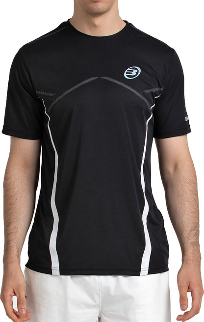 A man in a Bullpadel Cabore Men's Padel T-Shirt - Black from Bullpadel, featuring quick-drying fabric, white accents, and a small blue logo, pairs it with white shorts while standing against a plain background.