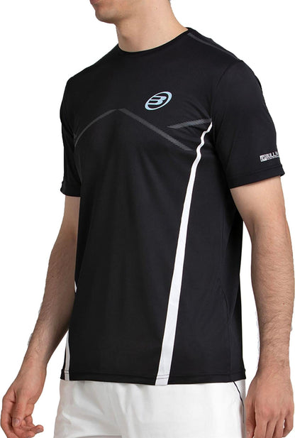 A man wears the Bullpadel Cabore Men's Padel T-Shirt in black by Bullpadel, featuring white accents and a small circular chest logo, paired with white shorts.