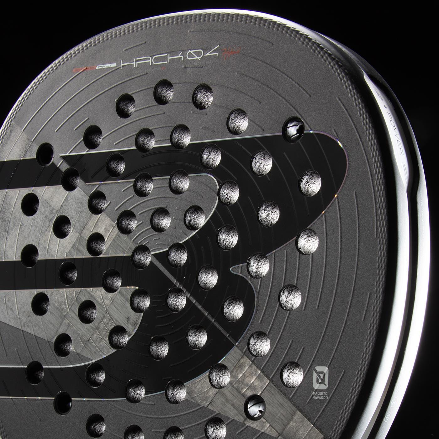 Close-up of the Bullpadel HACK 04 Hybrid 2026 Padel Racket in grey and black. Its circular holes, bold “B” logo, and “HACK 04” text highlight the dynamic design, with light reflecting off its modern frame for a powerful look.