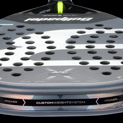 Close-up of the grey Bullpadel XPLO Comfort 2026 padel racket, highlighting its perforated surface, Bullpadel logo, and "Custom Weight System" label—engineered for explosive power and outstanding comfort with every shot.