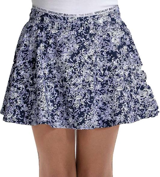 A person wearing the Bullpadel Parasil Women's Padel Skirt in Deep Ocean, featuring a navy and white scattered dot design, loose fit, and "THE PADEL SPECIALIST BULLPADEL" waistband text.