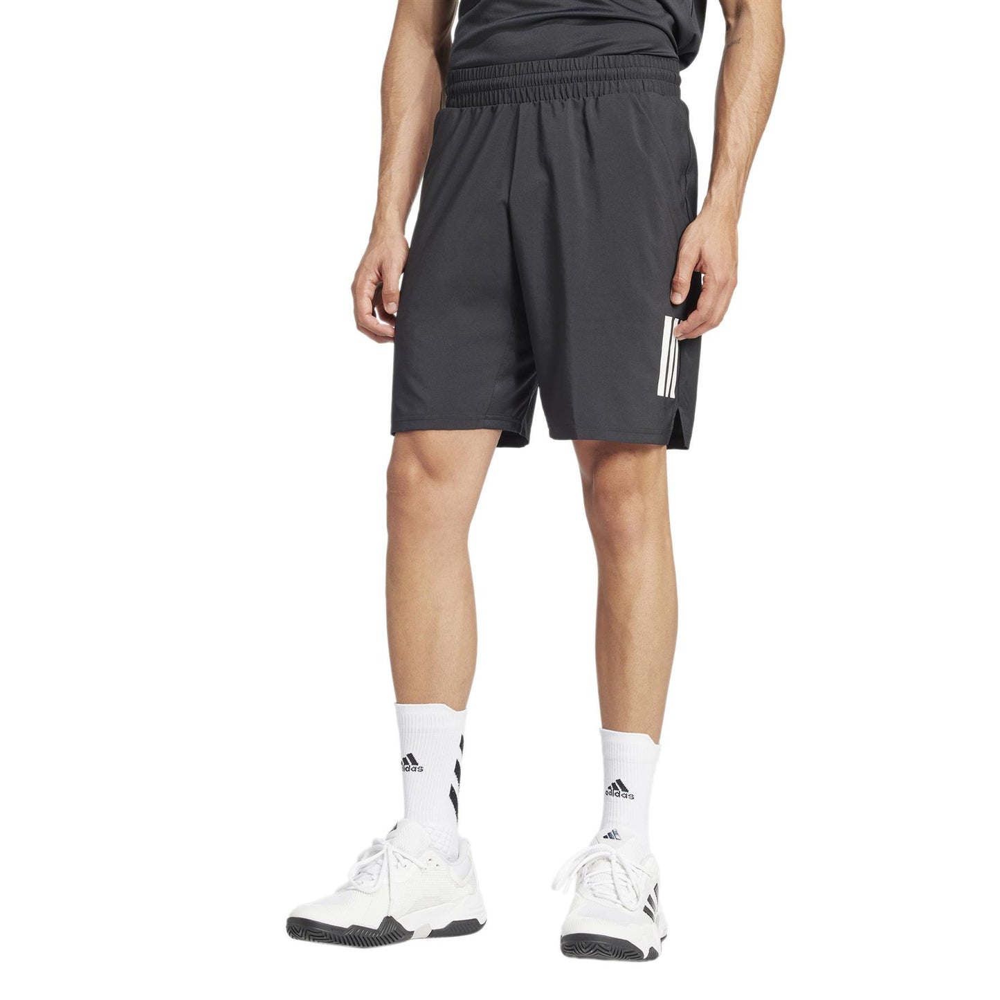 A person models ADIDAS Men's 3 Stripe Padel Shorts in black with white stripes and a moisture-wicking black shirt against a plain white backdrop, paired with white socks and sneakers.