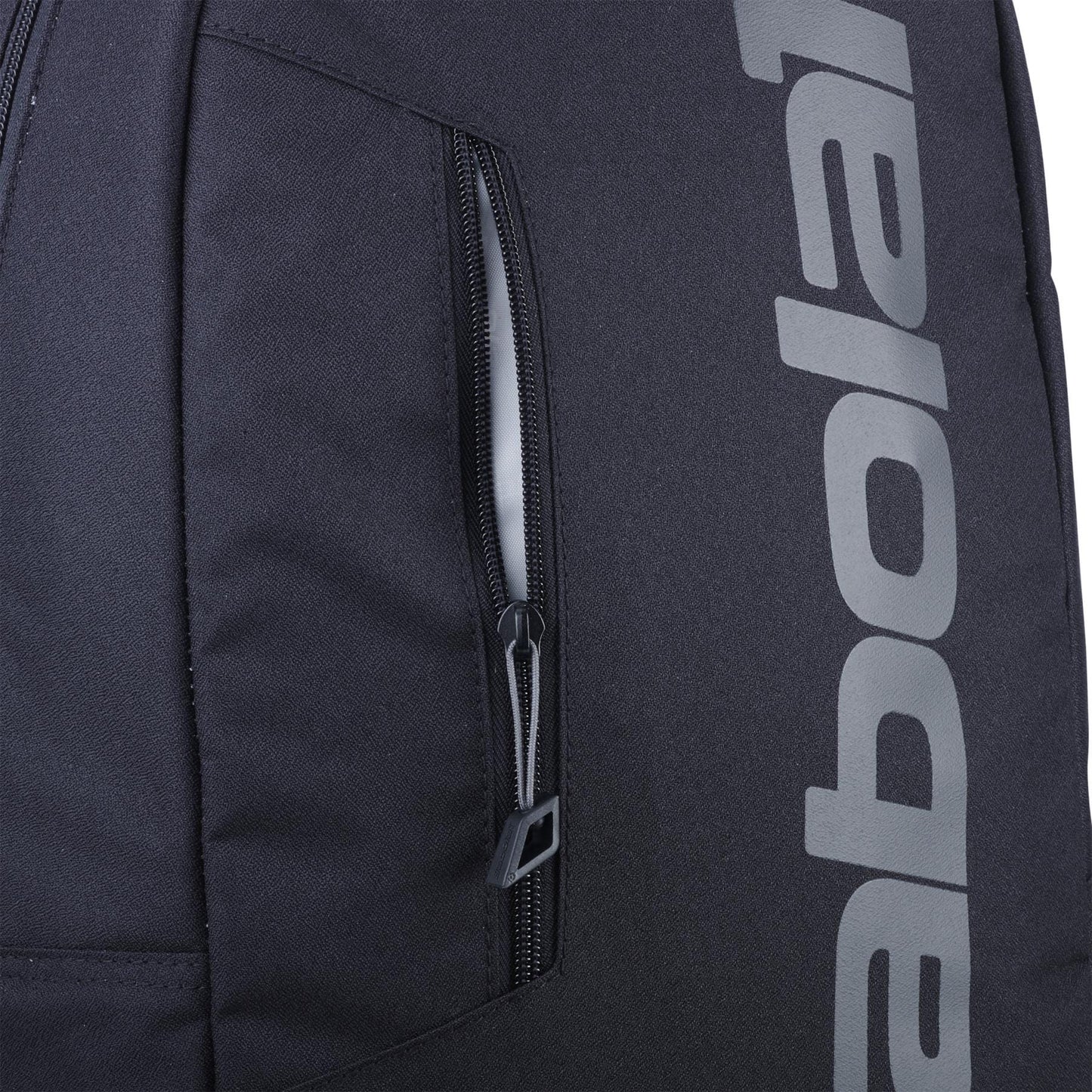 Close-up of the Babolat Court Lite Padel Backpack - Black by Babolat, showing a vertical zippered pocket and part of "babolat" in large light gray letters on the side; features a dedicated racket compartment for convenience.