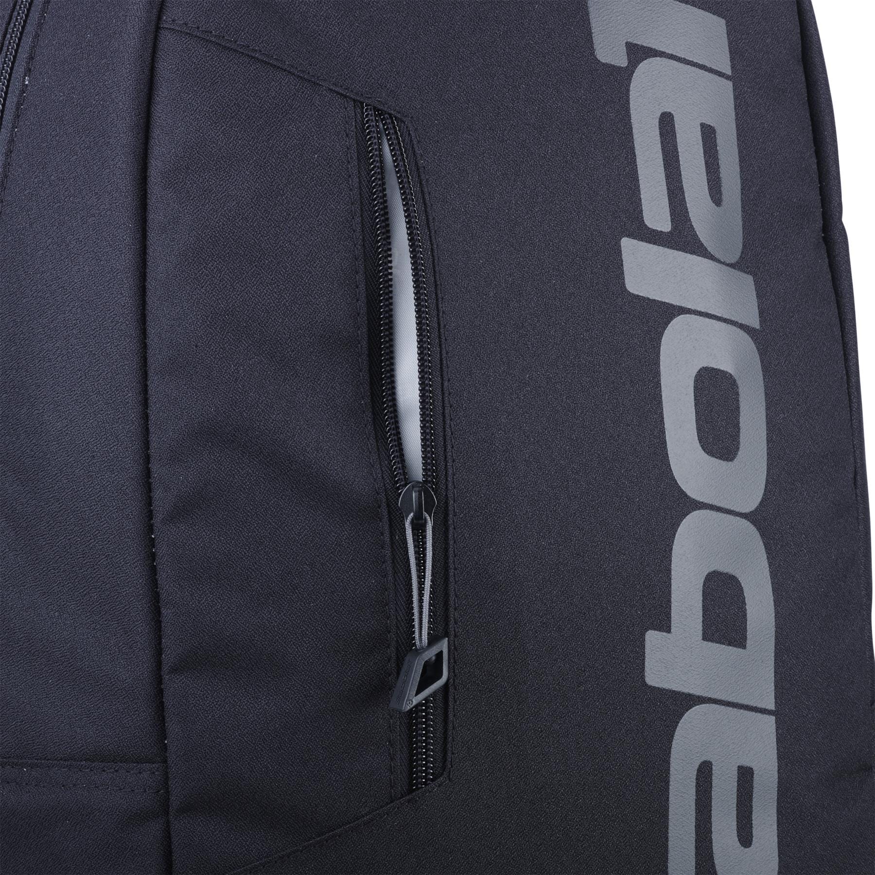 Close-up of the Babolat Court Lite Padel Backpack - Black by Babolat, showing a vertical zippered pocket and part of "babolat" in large light gray letters on the side; features a dedicated racket compartment for convenience.