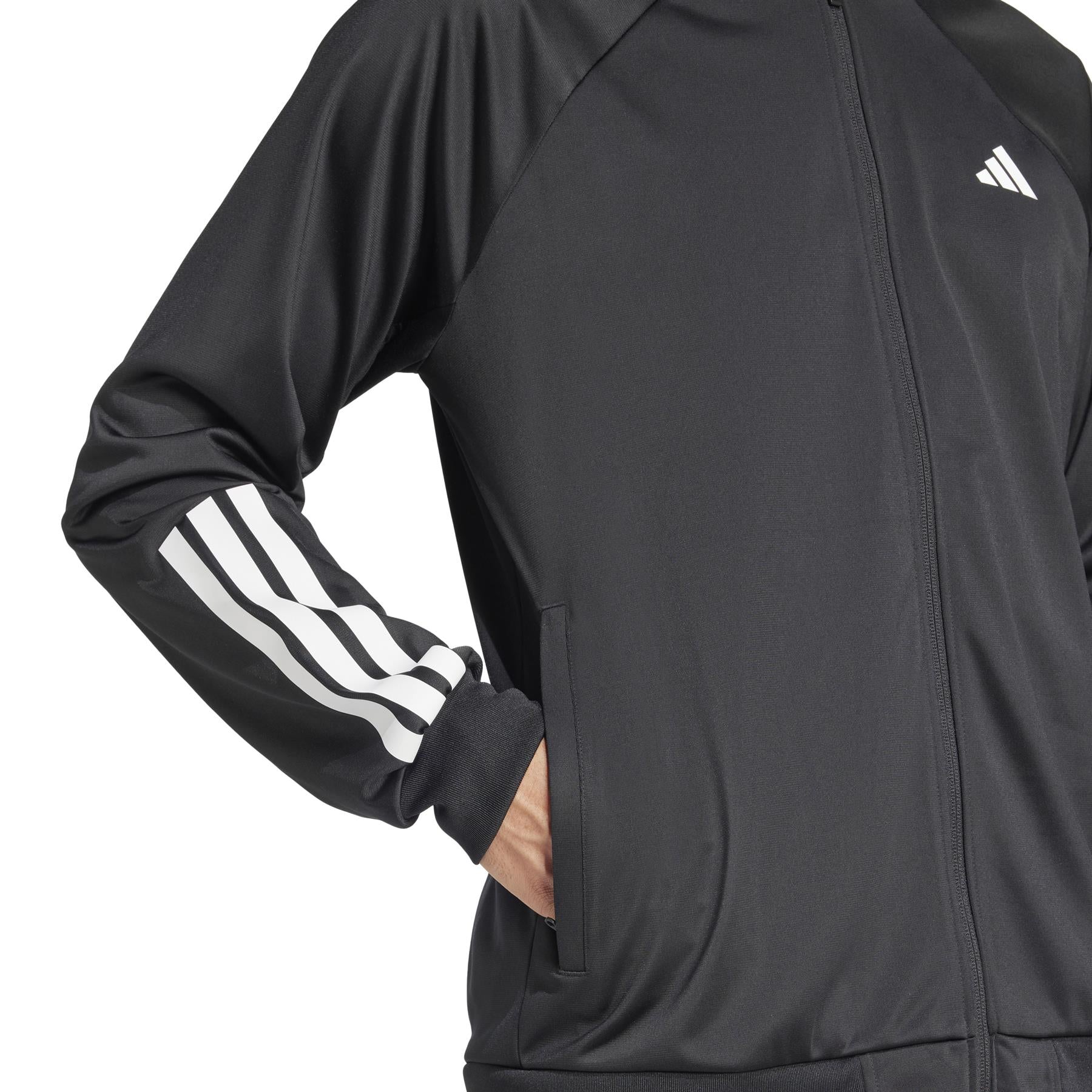 A person wears an ADIDAS Men's 3 Stripe Knit Padel Jacket in black, showcasing sleek white stripes on the sleeves and hands comfortably tucked into pockets.