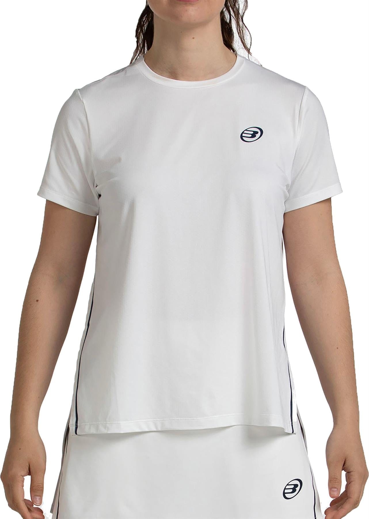 A woman wears the Bullpadel Picase Women's Padel T-Shirt in bone with a subtle navy logo on the left chest, paired with a matching white skirt. Her face isn’t visible in this Bullpadel performance padel outfit.