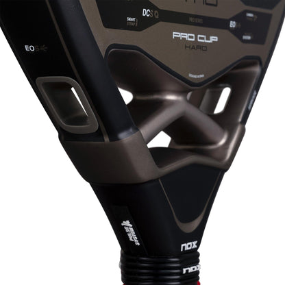 Close-up of the throat area of the NOX AT10 Pro Cup Hard By Agustín Tapia 2026 padel racket, showing NOX logos, holes, and part of the handle with wrist strap. The black metallic surface features white and gold accents.