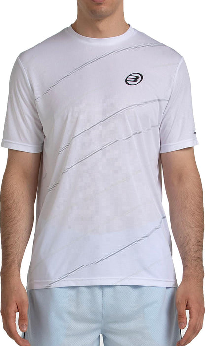 A man wears the Bullpadel Casinas Men's Padel T-Shirt in white, featuring subtle diagonal line patterns, a small black Bullpadel logo, and QuickerDry technology. He pairs it with light blue shorts; his face is not visible.