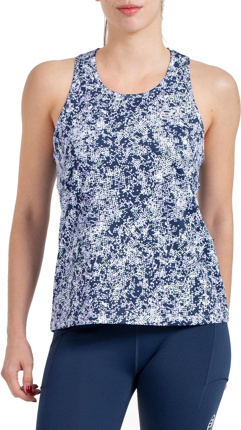 A woman stands against a white background wearing the Bullpadel Pilme Women's Padel Tank Top in Deep Ocean and navy leggings, showcasing stylish and breathable sportswear from Bullpadel.