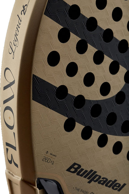 Close-up of a gold and black Bullpadel Flow 2027 padel racket, featuring the Bullpadel brand name on the edge, a diamond-shaped head, round holes, and a 3D Grain surface for enhanced grip. Balance and weight details are printed near the bottom.