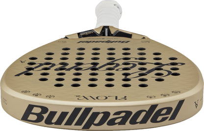 A Bullpadel Flow 2027 Padel Racket in gold, displaying a white grip, black Bullpadel logo, and round perforations on the face. The racket features a 3D Grain surface for enhanced control and is viewed from a low angle.