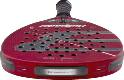 A close-up view of the red Bullpadel Hack 05 Comfort 2027 Padel Racket by Bullpadel highlights its perforated face, advanced Tricarbon 18K construction, custom weight system, and textured surface details, all featuring a responsive MultiEva core.