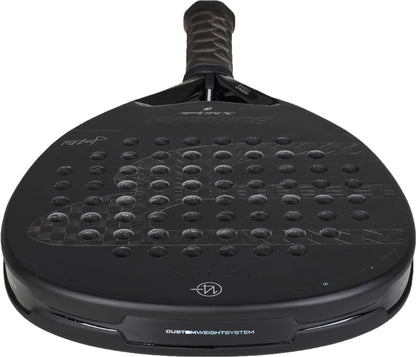 A close-up view of a black Bullpadel Icon 2027 Padel Racket, showcasing its textured X-Tend Carbon 12K surface with multiple circular holes, padded handle, MultiEva core, and Bullpadel branding details.